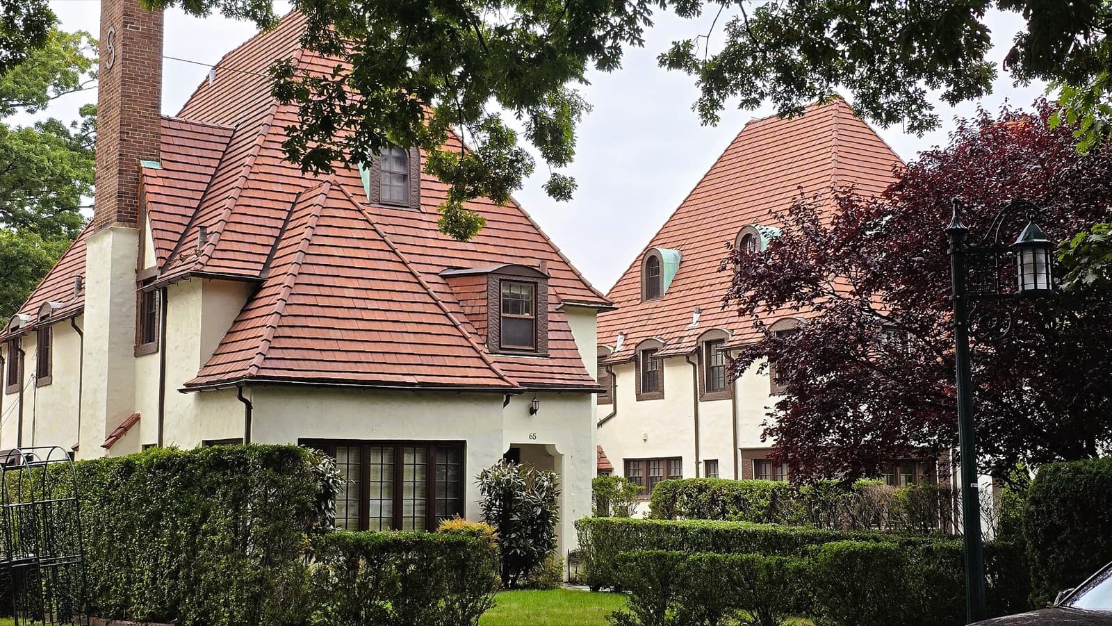 Two stucco Tudor-style homes behind hedges in Forest Hills Gardens